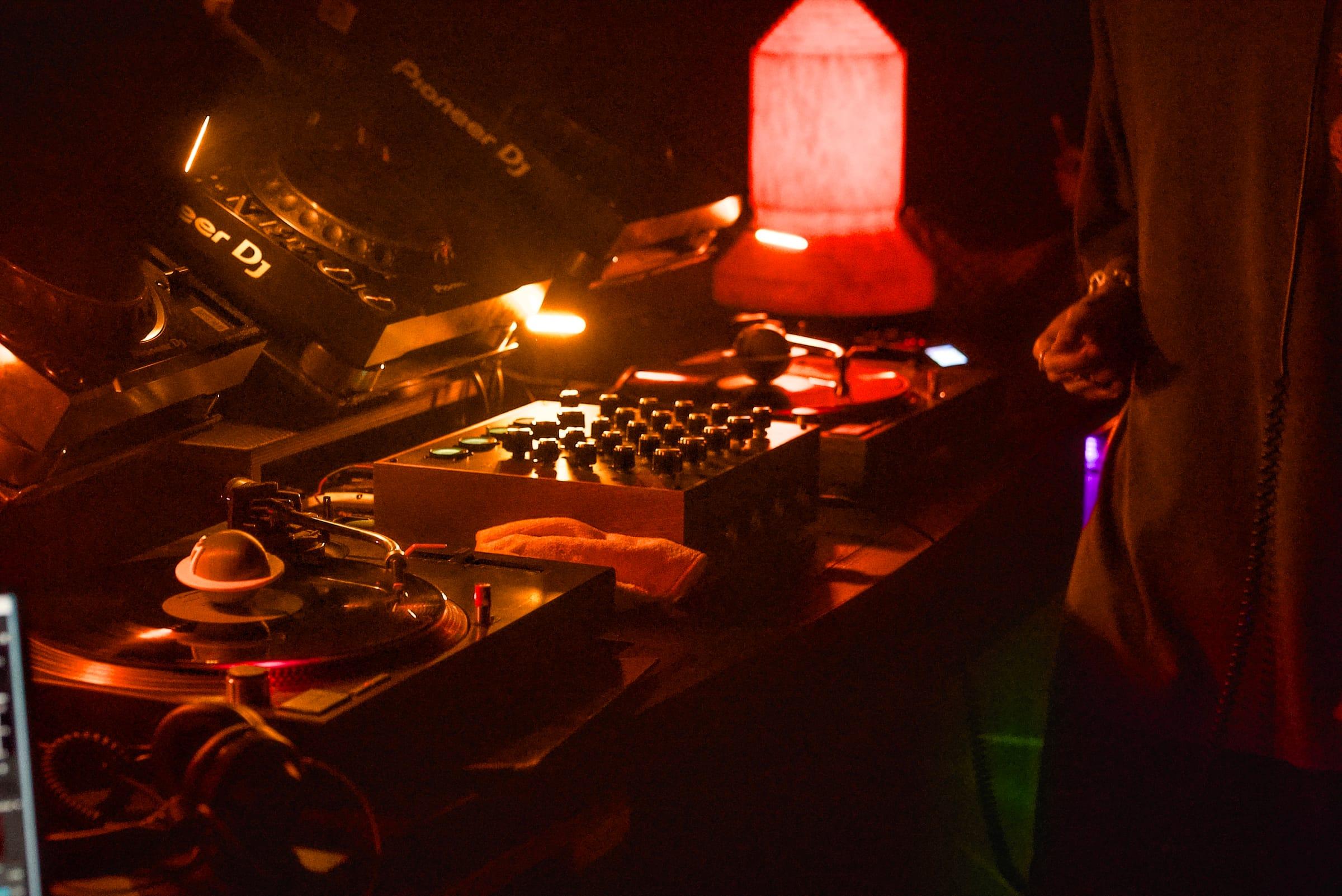 DJ mixer knobs glow under a red lamp beside a spinning record on the turntable.