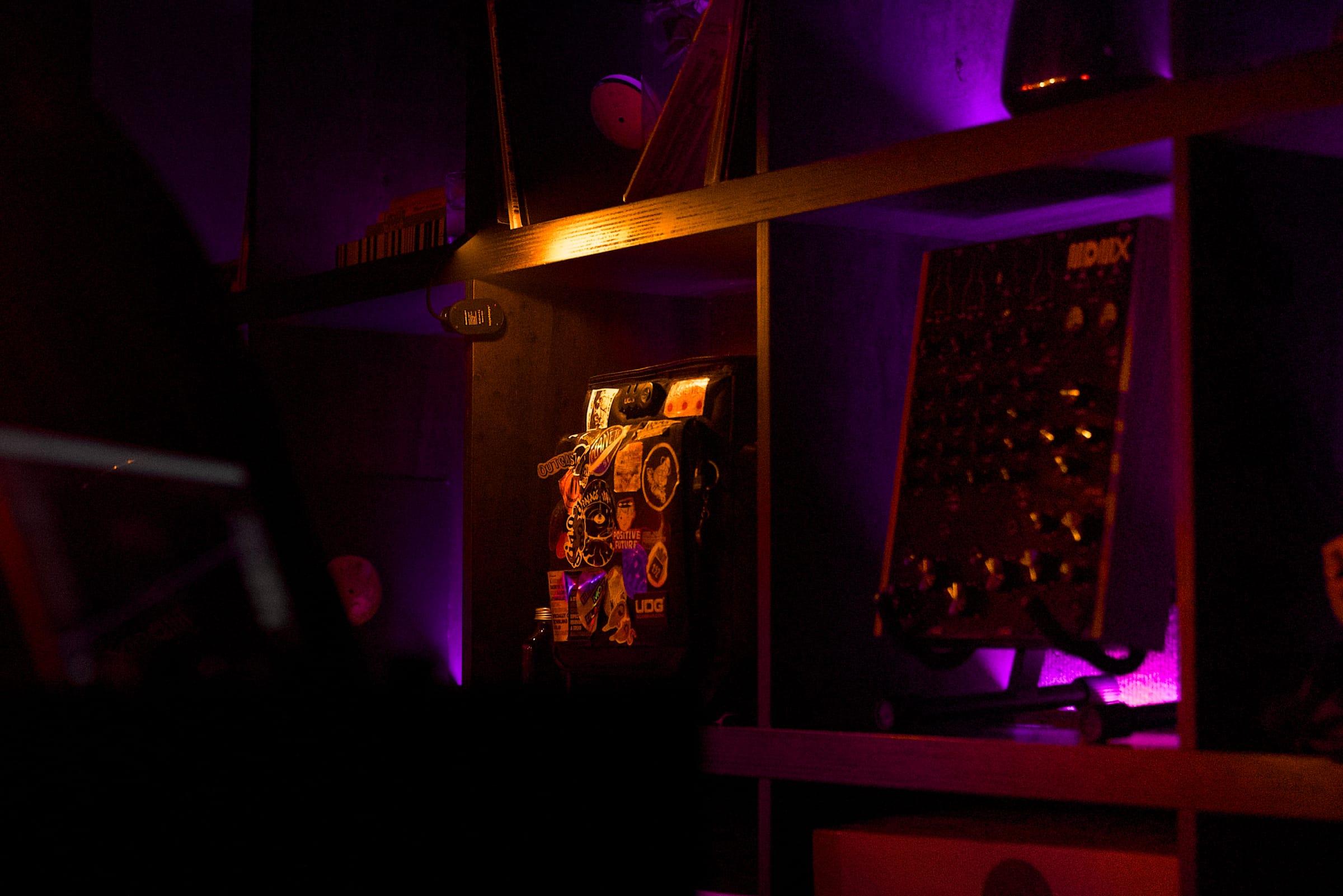 A sticker-covered flight case and gear cabinet on a shelf, lit in deep violet and red.